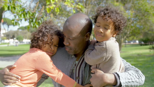 African-American-father-hugging-and-kissing-curly-children-in-park