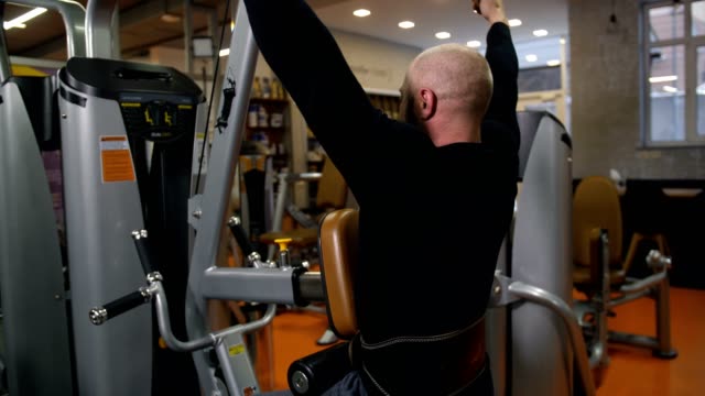 A-man-with-a-beautiful-body,-doing-an-exercise-on-the-simulator,-aimed-at-the-back-muscles.-View-from-the-back-4K-Slow-Mo