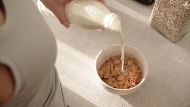 Gesundes-Frühstück.-Frau-Hand-gießen-Milch-in-Schüssel-mit-Flocken
