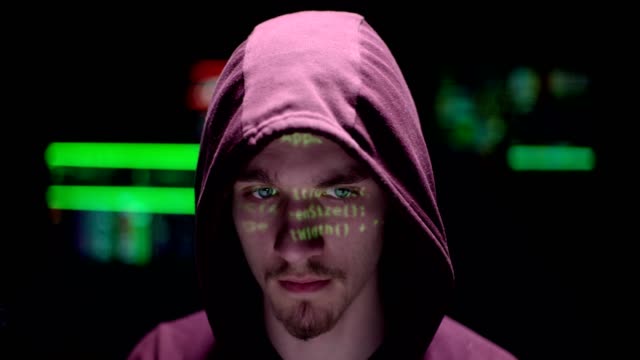 Close-up-on-a-men-with-a-hoodie-and-data-on-his-face,-screens-are-behind-him
