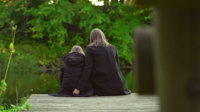 Woman-and-her-daughter-sitting-near-the-pond.