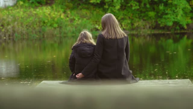 Woman-and-her-daughter-sitting-near-the-pond.