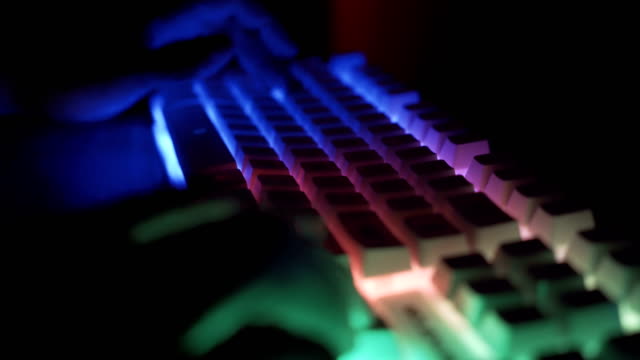 Männliche-Gamer-Tippen-und-Drücken-von-Tasten-auf-weißen-Gaming-RGB-Tastatur-in-dunklen-Raum