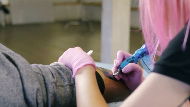 Artista-de-tatuaje-femenino-con-el-pelo-rosa-haciendo-tatuaje-en-el-estudio