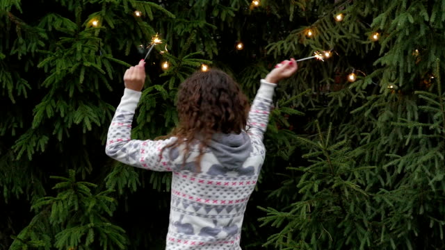 mujer-joven-en-el-fondo-del-árbol-de-Navidad-y-guirnaldas-con-sparklers.fun-y-saltos