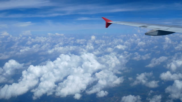 4K-footage.-traveling-by-air.-aerial-view-through-an-airplane-window.-wing-airplane-and-beautiful-white-clouds-in-blue-sky-for-background