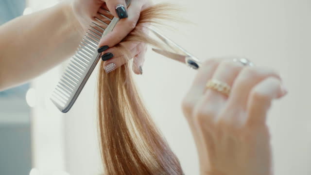 Female-hairdresser-cutting-hair-tips-with-hairdressing-scissors-in-beauty-salon.