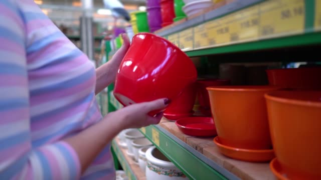 Caucasian-woman-near-shop-shelves-choosing-ceramic-pot-for-household-in-store-closeup