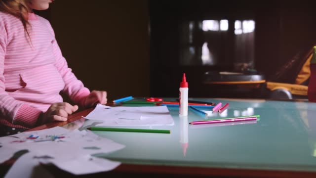 Camera-sliding-left-on-little-cute-Caucasian-girl-child-in-pink-sweater-drawing-with-a-pencil-at-table-with-stationery