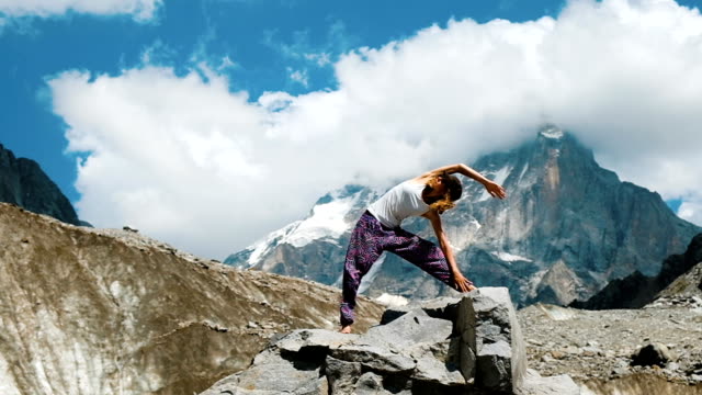 Mujer-se-dedica-a-la-gimnasia-yoga-sobre-fondo-de-una-montaña-de-nieve-en-una-excursión.-Chica-haciendo-estiramientos-al-aire-libre-en-una-caminata-al-aire-libre,-cámara-lenta