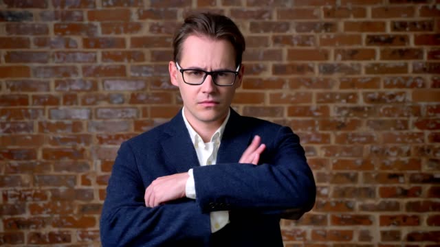 Serious-caucasian-man-in-business-suit-and-glasses-standing-and-looking-at-camera-focused-in-red-brick-studio-isolated