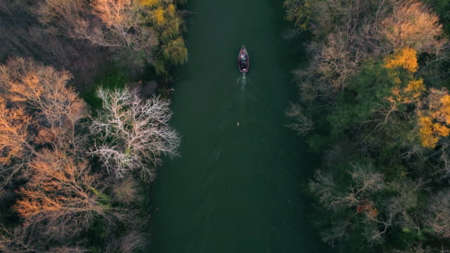River-and-autumn-trees-and-sailing-fishing-boat-during-sunset,-aerial-drone-video