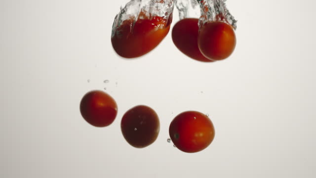 SLOW-MOTION:-Cherry-tomatoes-fall-under-water-on-white-background