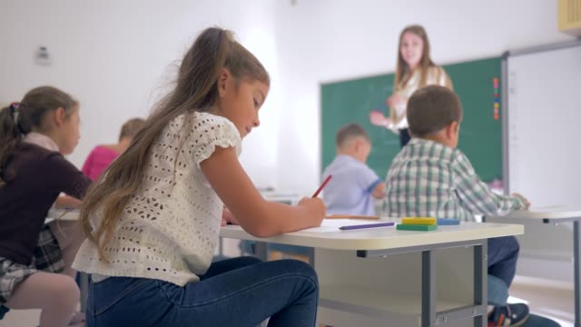 Porträt-der-schönen-Lernenden-Mädchen-am-Schalter-während-der-Lektion-im-Klassenzimmer-in-der-Grundschule-auf-unscharfen-Hintergrund