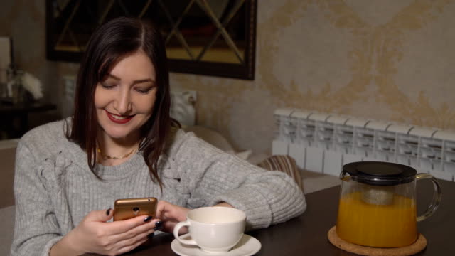 Frau-in-einem-Café-an-einem-Tisch,-trinken-Tee-und-blättert-in-einem-Band-von-sozialen-Netzwerken