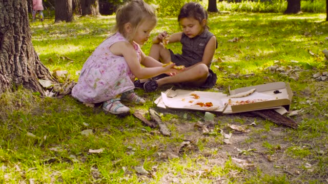 Zwei-Mädchen-im-Park-Pizza-essen.