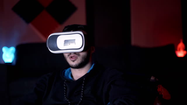 Jugador-masculino-poniendo-gafas-de-realidad-virtual-en-la-cabeza-y-empezar-a-jugar-con-el-controlador,-sentado-en-el-sofá