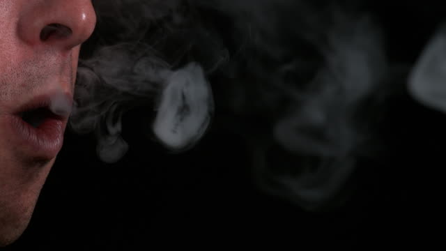Hombre-fumando-un-cigarrillo-contra-el-fondo-negro,-lenta-de-4K