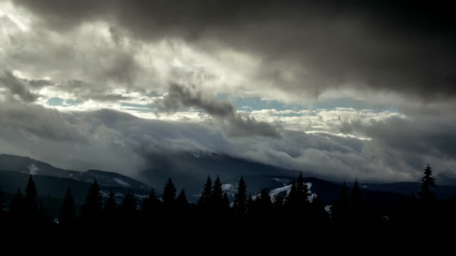 Time-lapse-thunder-clouds-moving-above-winter-mountain-range-dark-pine-forest-foreground-nature-landscape