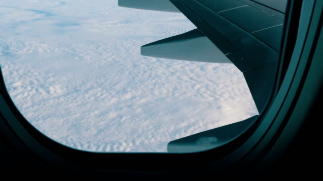 Wing-of-the-plane-through-the-porthole.-The-plane-flies-over-beautiful-air-clouds