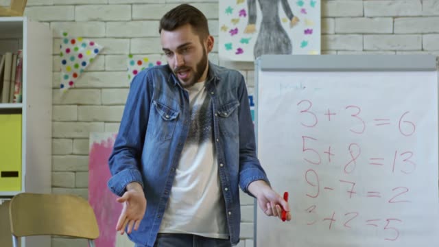 Male-Teacher-Writing-on-Whiteboard-at-Math-Lesson-in-Kindergarten
