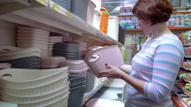 Caucasian-woman-near-shop-shelves-choosing-plastic-basket-in-store