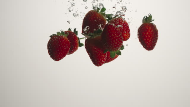 SLOW-MOTION:-Strawberries-fall-in-water-on-white-background