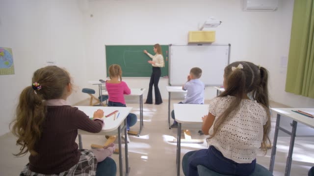 Kinder-Schulbildung,-führt-junge-Lehrerin-Frau-in-der-Nähe-von-Blackboard-kognitive-Lektion-für-kleine-Kinder-am-Schreibtisch-im-Klassenzimmer-der-Schule