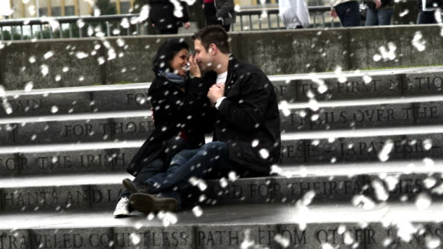 A-couple-sits-on-some-steps-in-front-of-a-fountain-while-holding-hands