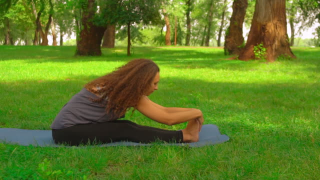slim-woman-does-forward-bend-pose-in-park