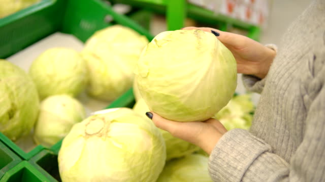 Young-woman-in-the-vegetable-department-of-a-supermarket-chooses-a-cabbage
