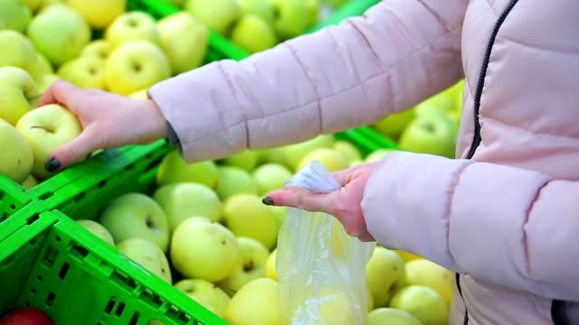 Closeup-of-the-hand-of-a-woman-in-winter-clothes-putting-green-apples-in-a-package.-She-chooses-the-most-delicious-and-fresh-fruit.