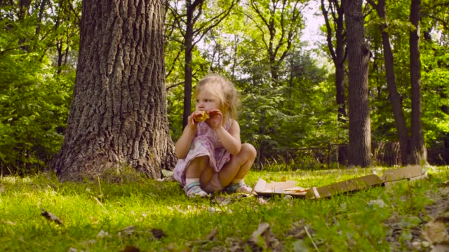 Little-girl-sitting-in-the-park-and-eating-pizza