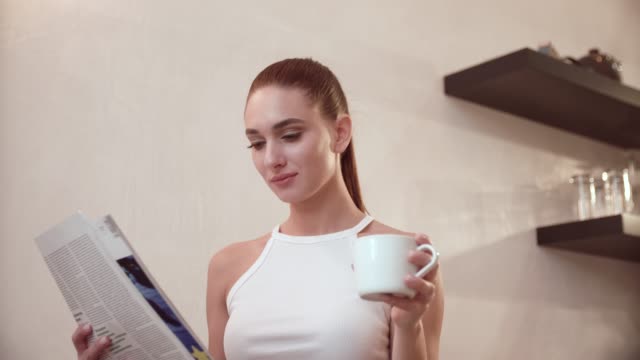 Woman-With-Newspaper-Drinking-Coffee-At-Breakfast-On-Kitchen