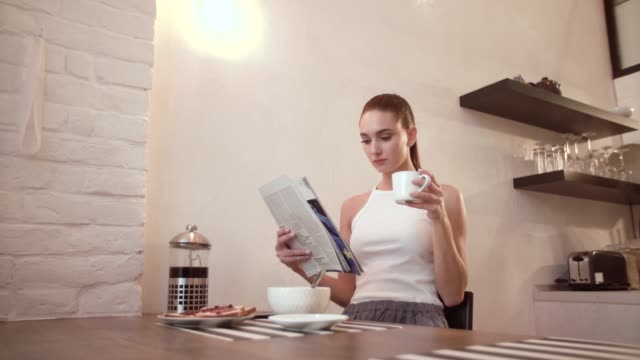 Mujer-con-periódico-de-beber-café-en-el-desayuno-en-la-cocina