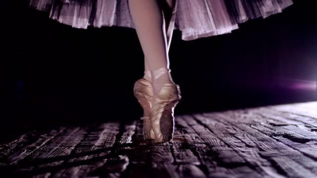 close-up,-in-rays-of-spotlight,-on-stage-of-old-theater-hall.-ballerina-in-white-ballet-skirt,-raises-on-toes-in-pointe-shoes,-performs-elegantly-a-certain-ballet-exercise,-en-tournaht-suivi