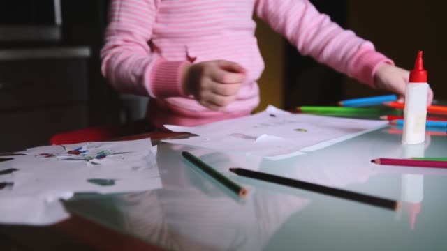 Cámara-deslizante-derecha-mostrando-niño-niña-Europea-en-suéter-rosa-tomando-un-lápiz-para-dibujar-en-la-mesa-con-artículos-de-papelería