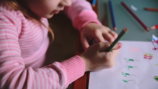 Camera-sliding-right-over-cute-Caucasian-little-girl-drawing-on-paper-with-different-color-pencils-at-a-table-close-up