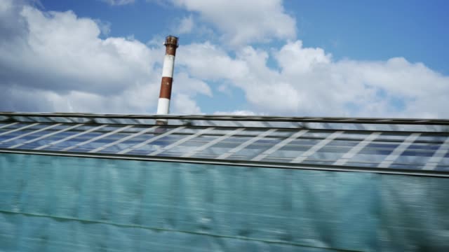 Car-view-tracking-shot-of-large-glass-greenhouses-of-modern-farm-and-blue-sky-with-clouds-above-them