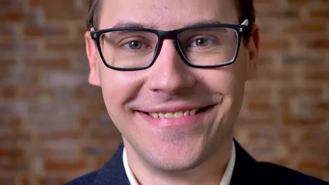 Calm-confident-face-of-caucasian-businessman-in-glasses-looking-at-camera-focused-next-to-the-brick-wall