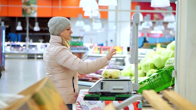 Frau-in-Winterkleidung-im-Supermarkt-Äpfel-auf-Waage-wiegen.-Sie-wählt-den-Code-und-den-Wert-der-Frucht.