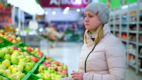 Woman-in-winter-clothes-picks-fruit-in-a-supermarket.-She-looks-apples.