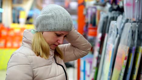 Eine-Frau-mittleren-Alters-in-einen-Hut-und-eine-Daunenjacke-wählt-waren-im-Supermarkt.