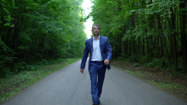 young-businessman-in-a-blue-suit-is-walking-along-the-road-in-forest