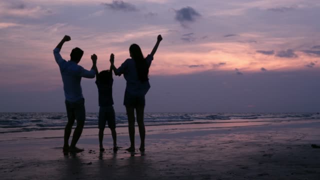 SLOW-MOTION,-familia-asiática-silueteado-mirando-al-atardecer-con-feliz-emoción-en-la-playa-juntos.-Concepto-de-familia,-vacaciones-y-viajes.