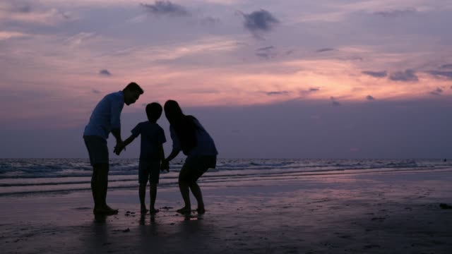 SLOW-MOTION,-Silhouetted-Asian-family-looking-to-sunset-with-happy-emotion-at-Beach-together.-Family,-Holiday-and-Travel-concept.