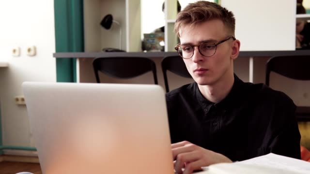 Junger-Mann-Student-in-Gläsern-mit-Laptop-im-Klassenzimmer