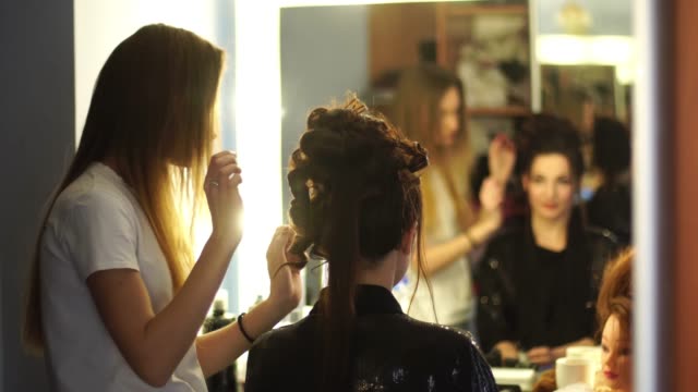 Young-blonde-stylist-girl-makes-hairstyle-to-a-woman