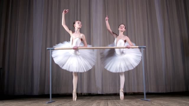 ballet-rehearsal,-in-old-theater-hall.-Young-ballerinas-in-white-ballet-skirts,-tutus,-are-engaged-at-ballet,-perform-elegantly-a-certain-ballet-exercise,-pass-,-attidude,-standing-near-barre