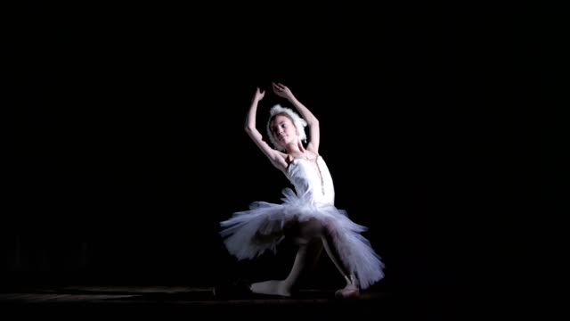 in-rays-of-spotlight,-on-the-stage-of-the-old-theater-hall.-Young-ballerina-in-suit-of-white-swan-and-pointe-shoes,-dances-elegantly-certain-ballet-motion,-part-de-bras